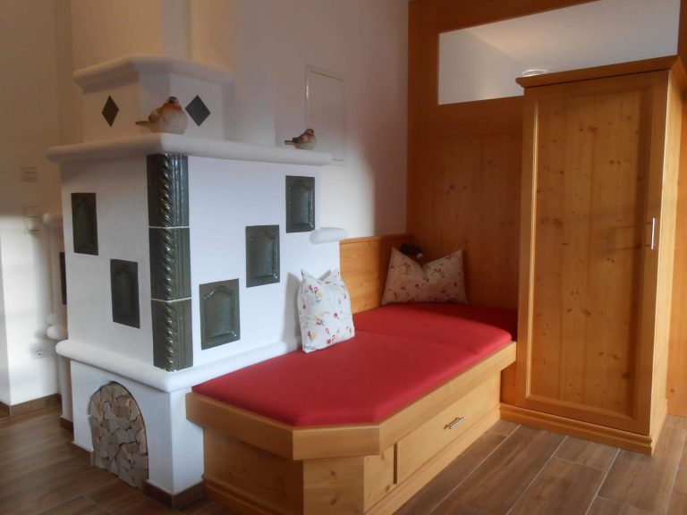 Gemütliche Ecke mit Kachelofen und roten Sitzpolstern im Ferienappartement am Gollehenhof.